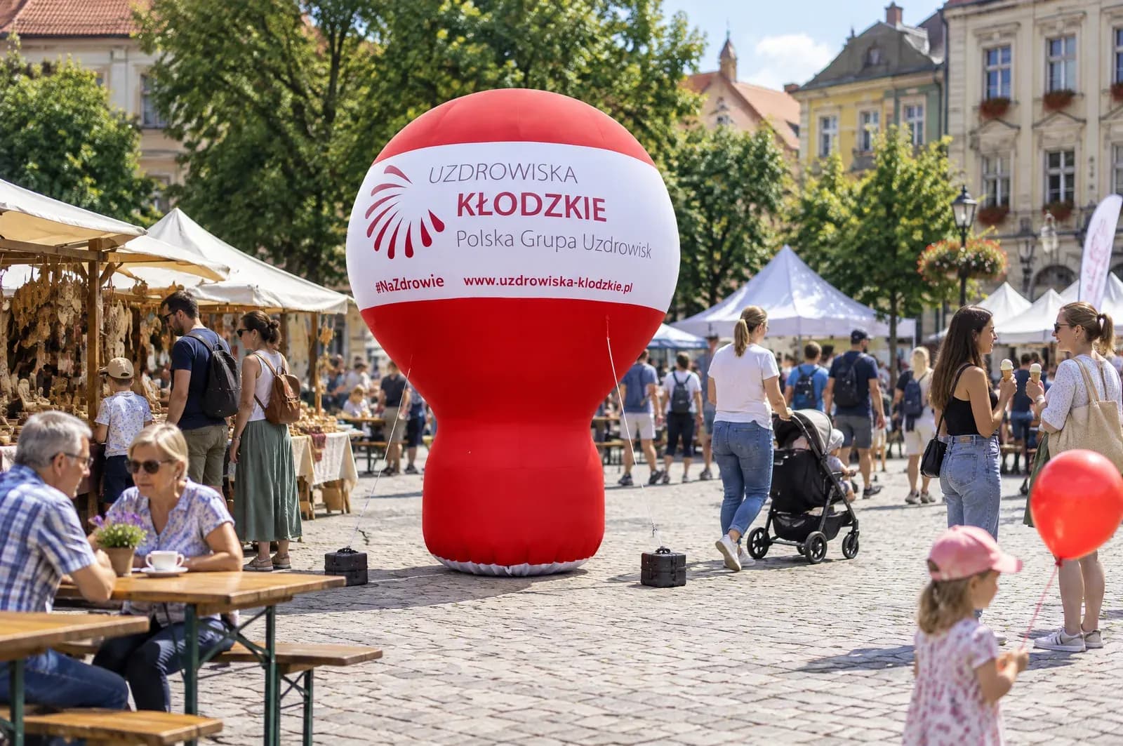 Balon reklamowy z talią Uzdrowiska Kłodzkie na rynku podczas festynu, obok stoiska i stoliki