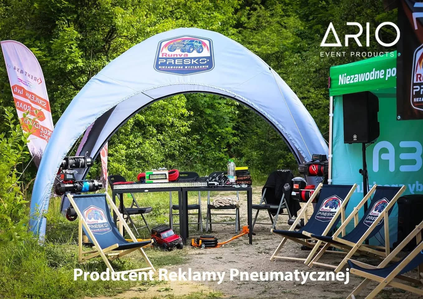 Namiot pneumatyczny i leżaki Presko na rajdzie terenowym Namiot pneumatyczny Presko z logo na poszyciu, przed nim leżaki reklamowe i nagłośnienie na leśnej polanie.